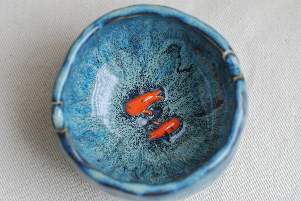 Ceramic ashtray with blue glaze and orange koi fish inside kept against a white background. made in the netherlands by pipa pots