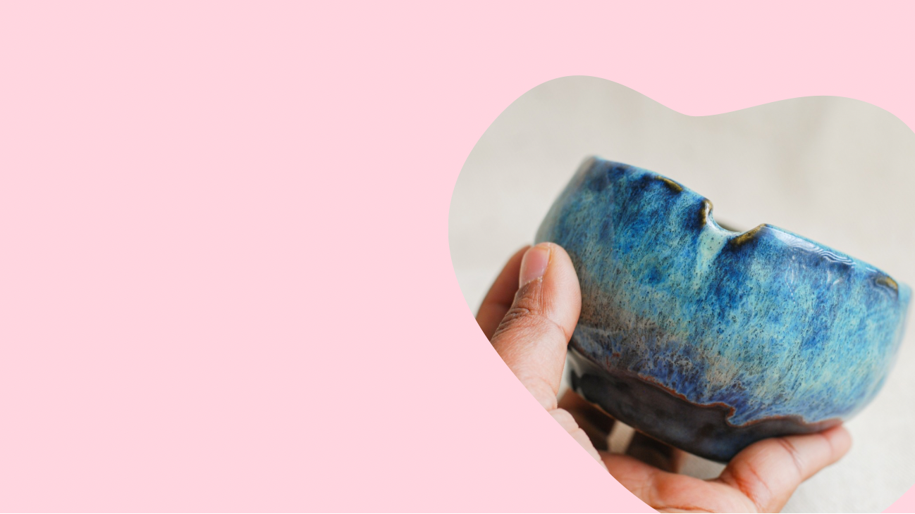 Hand holding a blue ceramic ashtray bowl made by pipa pots against a pink background