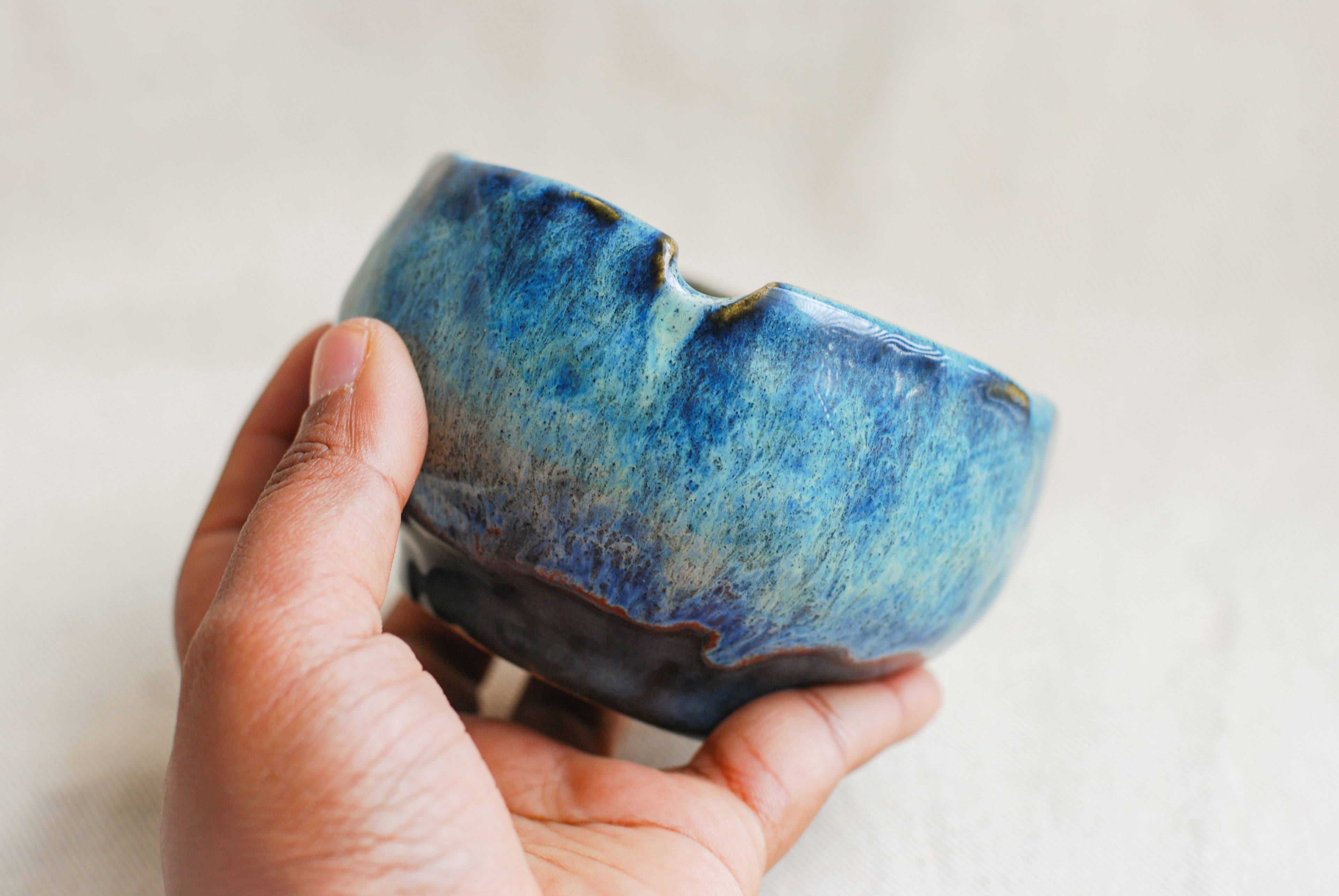 Hand holding a blue ceramic ashtray against a plain background. ashtray made in amsterdam by pipa pots