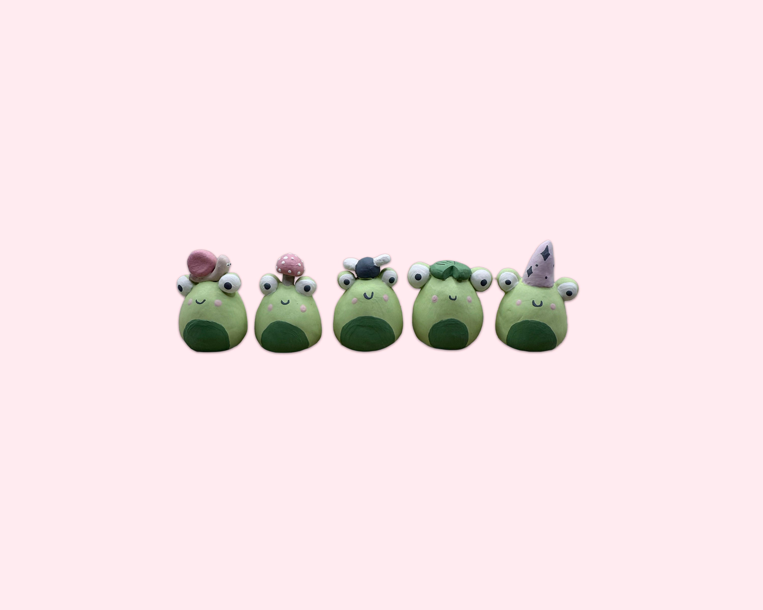 Five green frog figurines with various accessories on a white background made by pipa pots