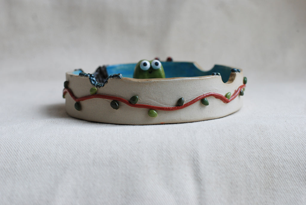 Ceramic ashtray made by pipa pots features a cute frog poping out with decorative elements on a white background