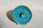 Ceramic frog on a blue circular plate with green rim against a light background