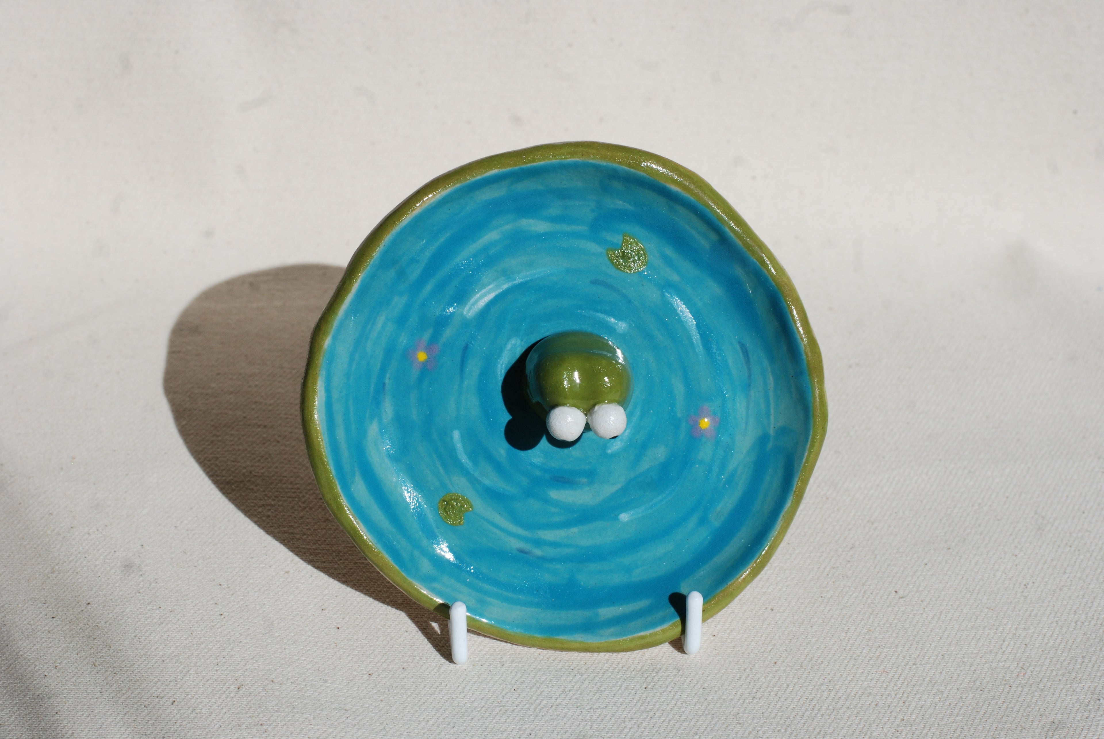 Ceramic frog on a blue circular plate with green rim against a light background