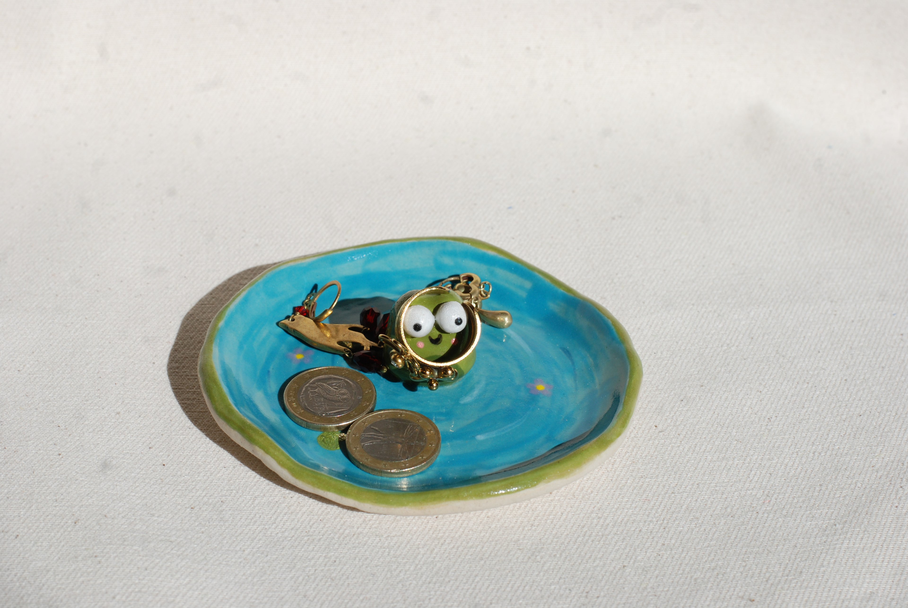 Small decorative dish with a frog who has googly eyes on a blue dish with coins. made by pipa pots in the netherlands
