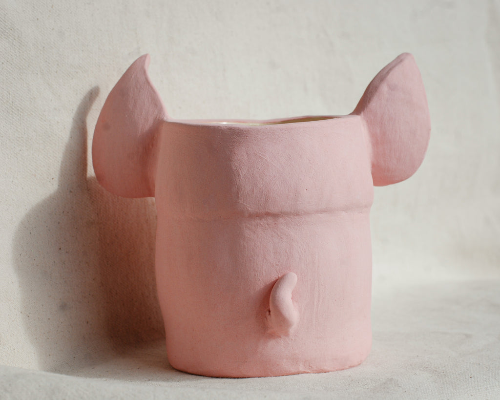 A pink ceramic planter shaped like an elephant head, featuring large ears on top and a small trunk detail on the front, set against a textured off-white background.
