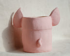 A pink ceramic planter shaped like an elephant head, featuring large ears on top and a small trunk detail on the front, set against a textured off-white background.