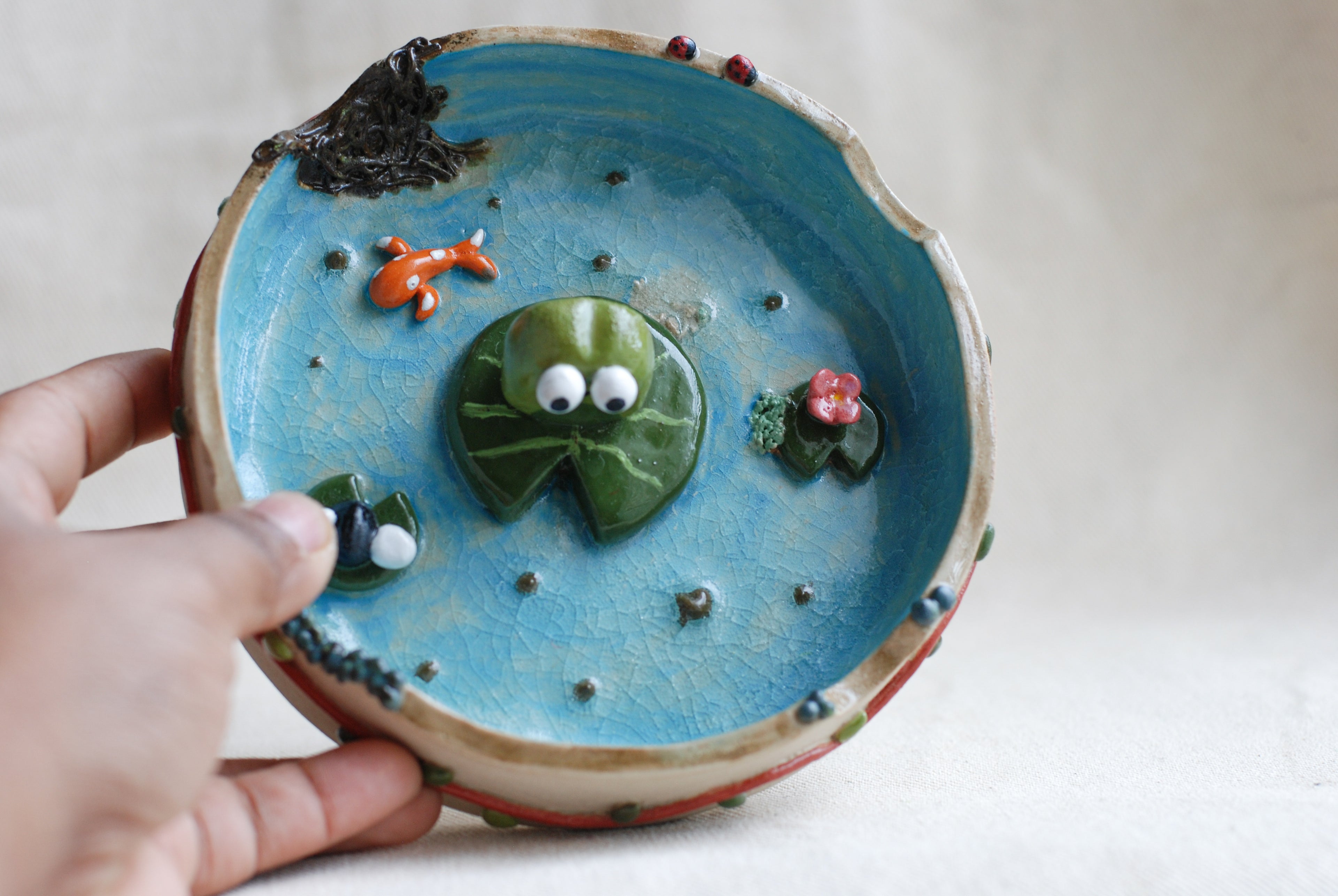 Ceramic ashtray with decorative elements held by a hand on a plain background made by pipa pots