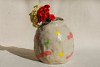 Ceramic vase with colorful star patterns and flowers on a neutral background